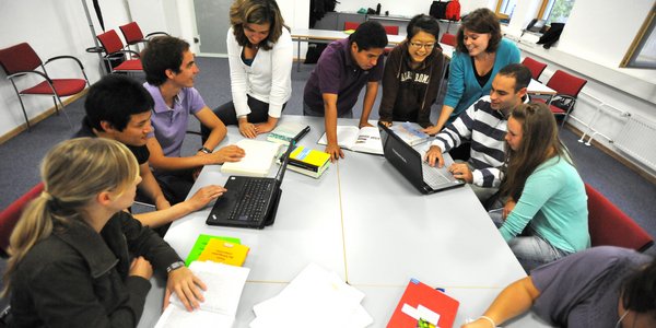 Studierendenteams bei der Projektarbeit um einen großen Arbeitsplatz versammelt